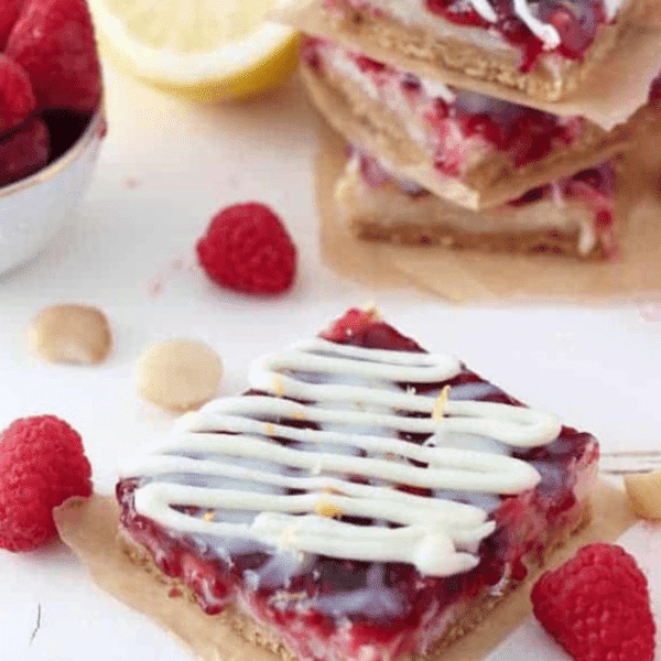 A scrumptious Lemon Raspberry Magic Cookie Bar with layers of shortbread crust, lemon zest, and raspberry jam, drizzled with white chocolate ganache.