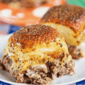 Delicious party roast beef sandwiches with melted cheese and a tangy sauce on a platter, ideal for game day or casual gatherings.